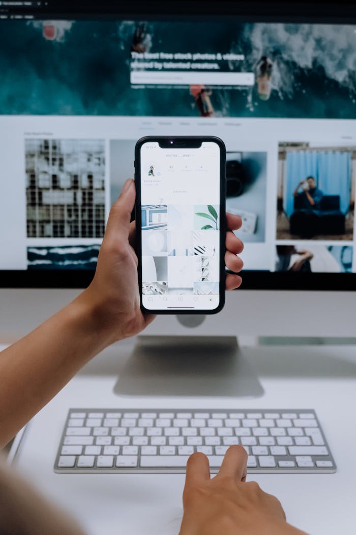 about-04 Person uses a smartphone in front of a computer screen displaying stock photos, showcasing modern technology use.